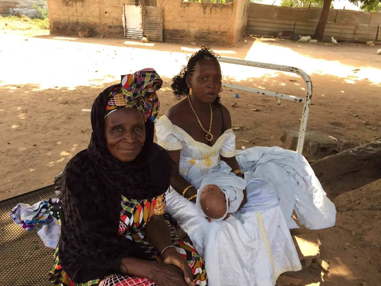 An older woman and a young mother with her newborn sitting together outdoors in the village