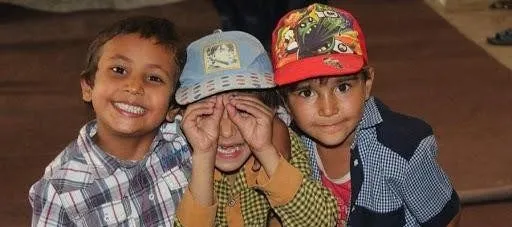 Three young boys smiling at the camera, two of them wearing caps