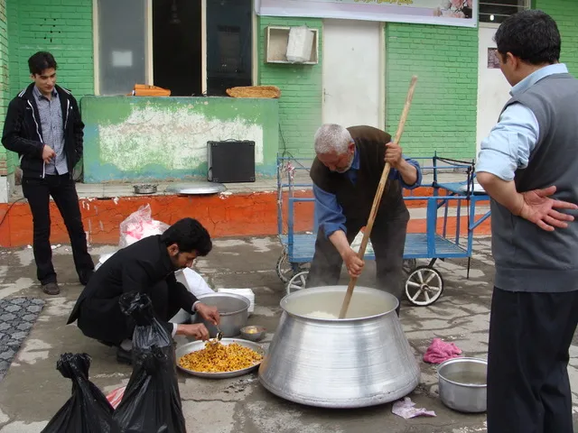 Men cooking rice in a large pot in the yard and portioning meals onto trays