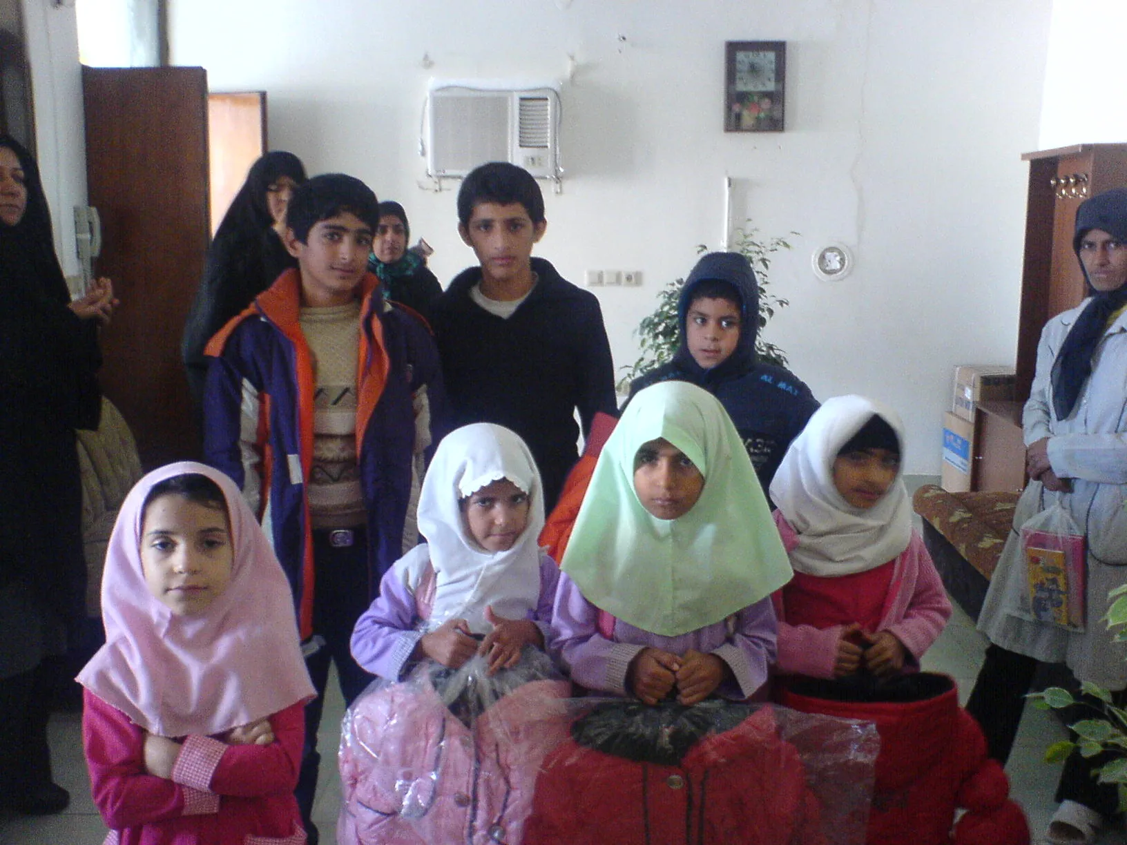 Children in winter coats and headscarves standing with newly delivered clothing still in its packaging