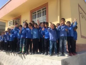 Boys in blue school uniform standing on a step outside the school, waving