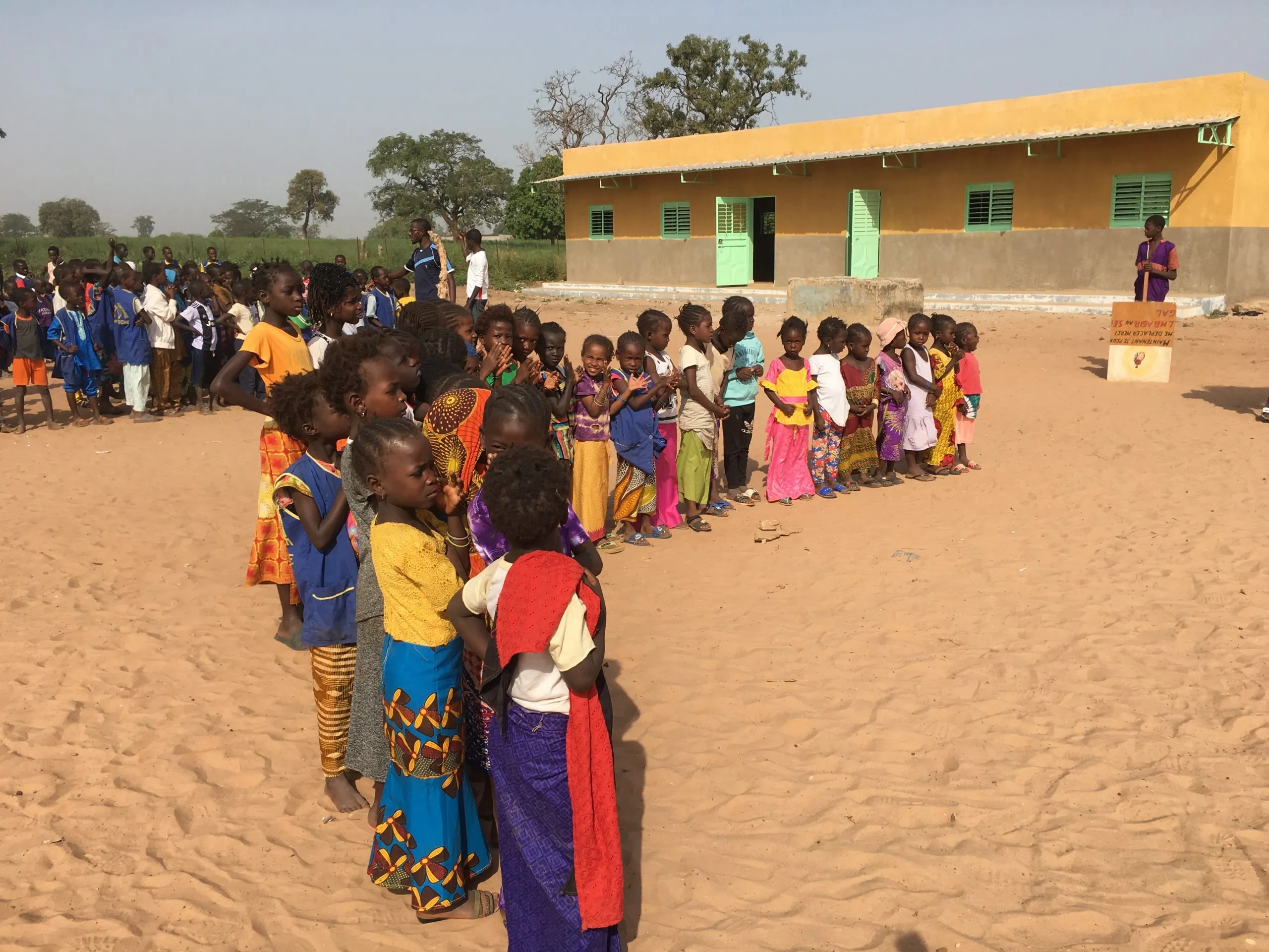 Children lined up on the sand in front of the new yellow school building