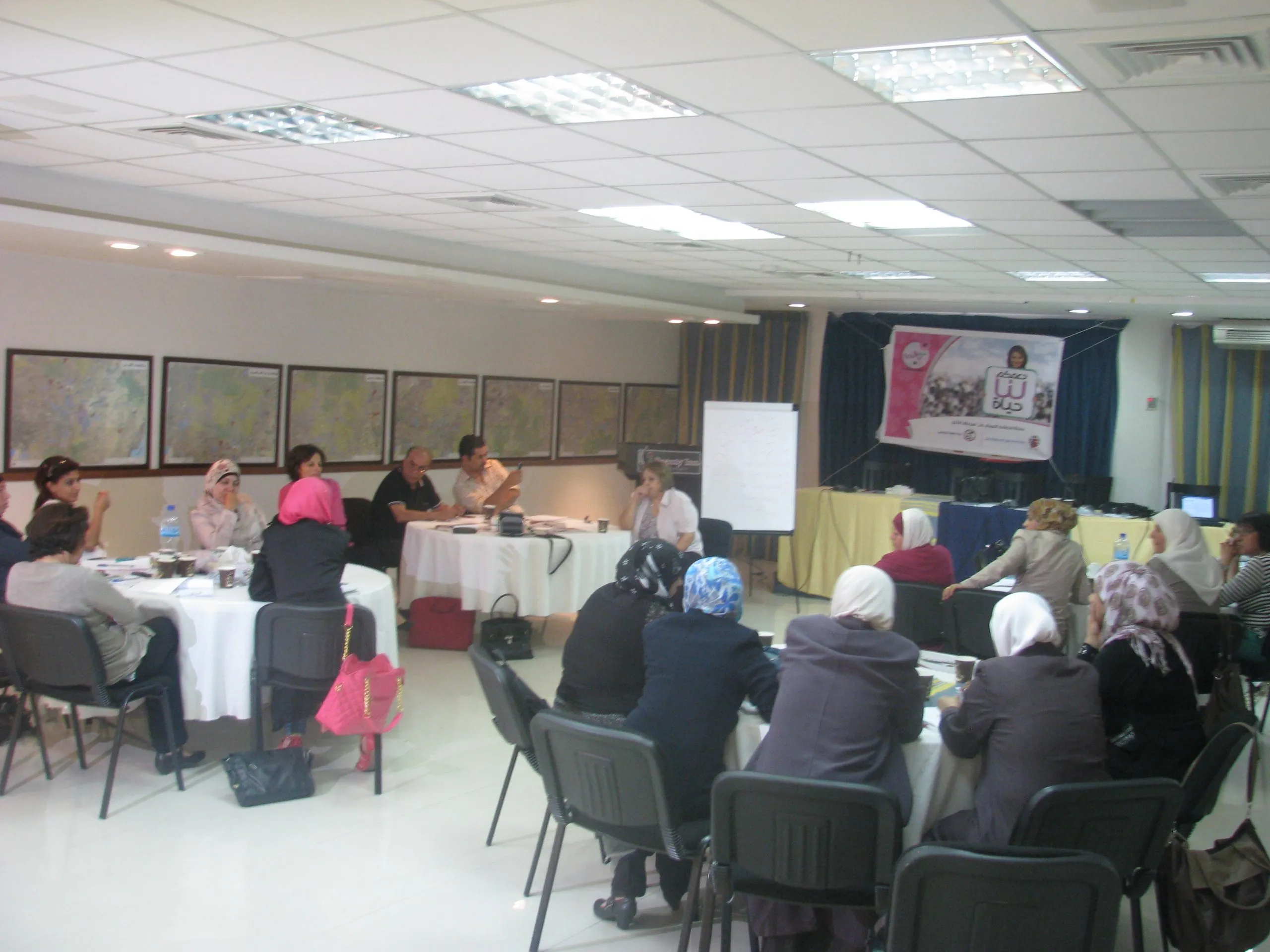 A training session in a conference room, women seated at round tables beneath a breast-cancer awareness banner