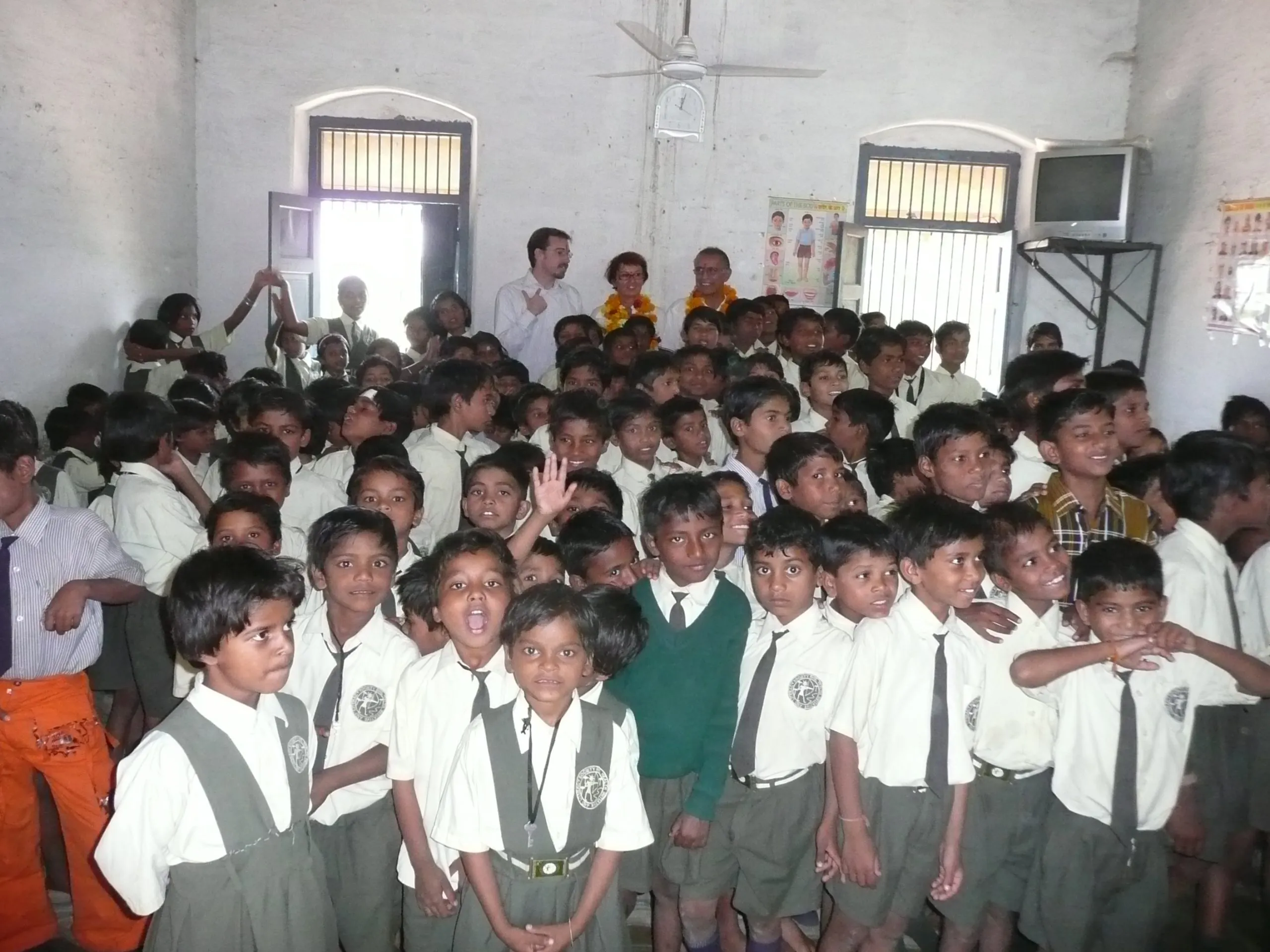 A large group of pupils in school uniform with three visitors wearing marigold garlands standing at the back