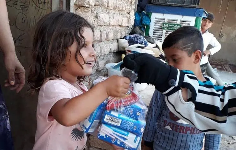 A girl handing packs of toothbrushes and toothpaste to a boy during a distribution