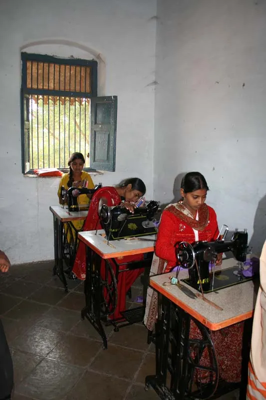 Three young women working at treadle sewing machines in the sewing class