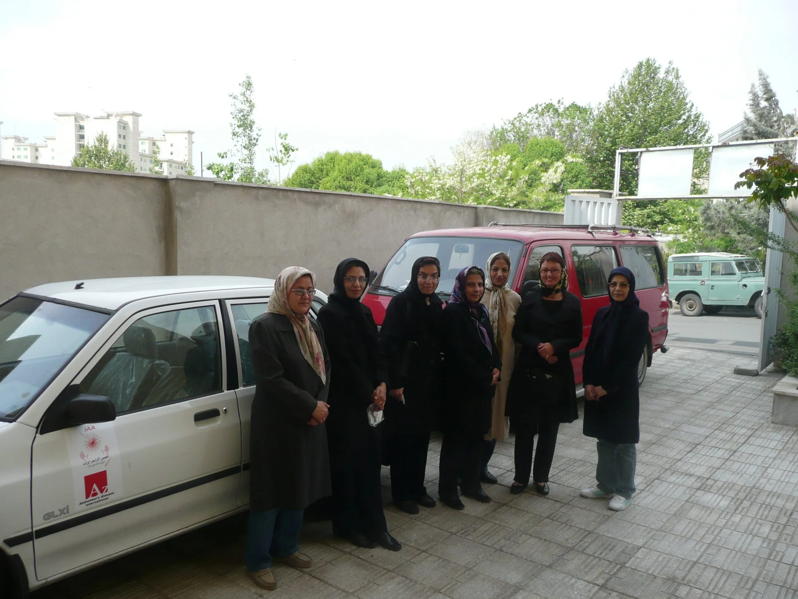 Staff of the Iran Alzheimer Association standing beside the association's cars in the courtyard