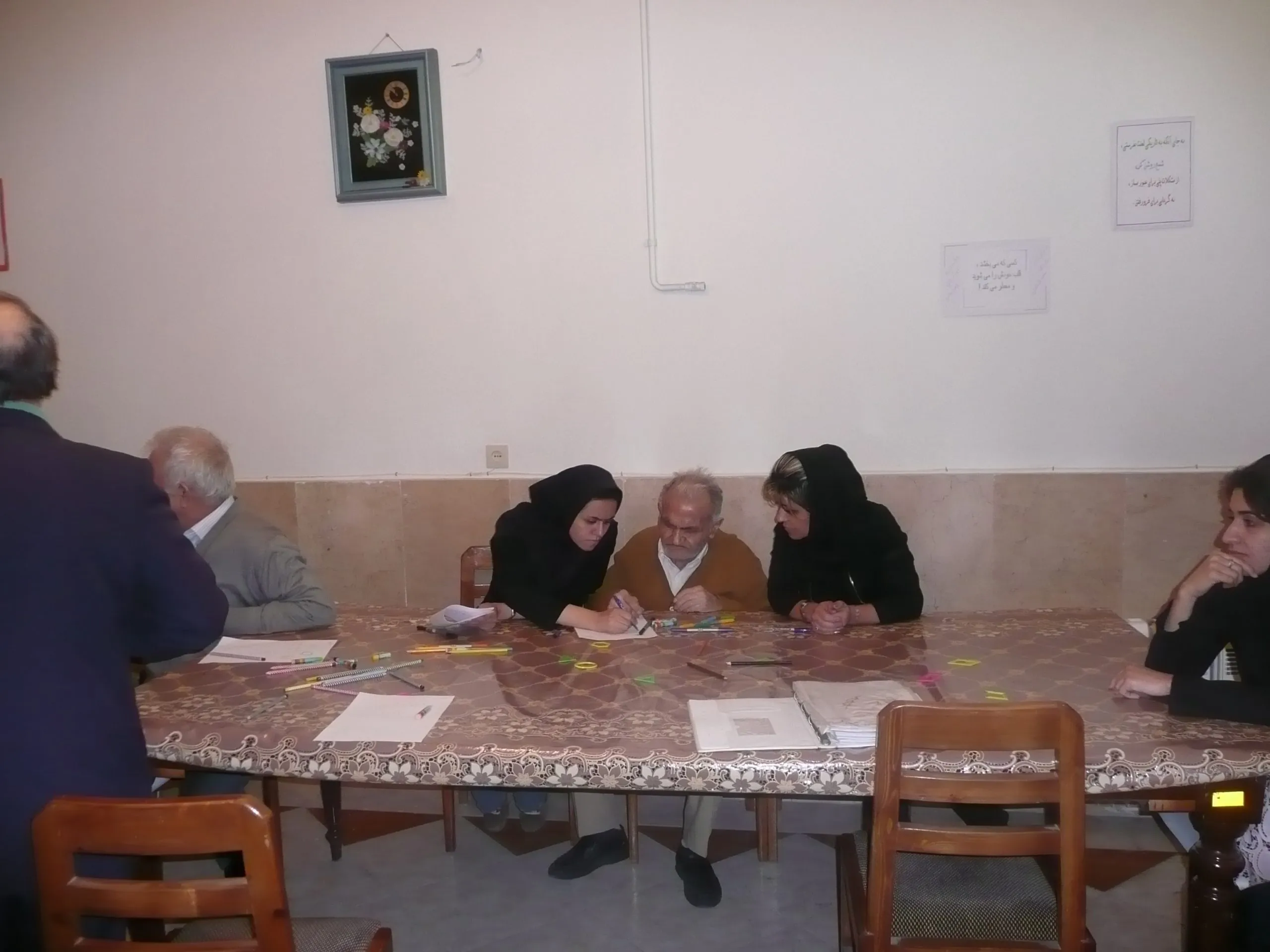Carers working with an elderly man at a table laid out with coloured pens and paper for a therapy session
