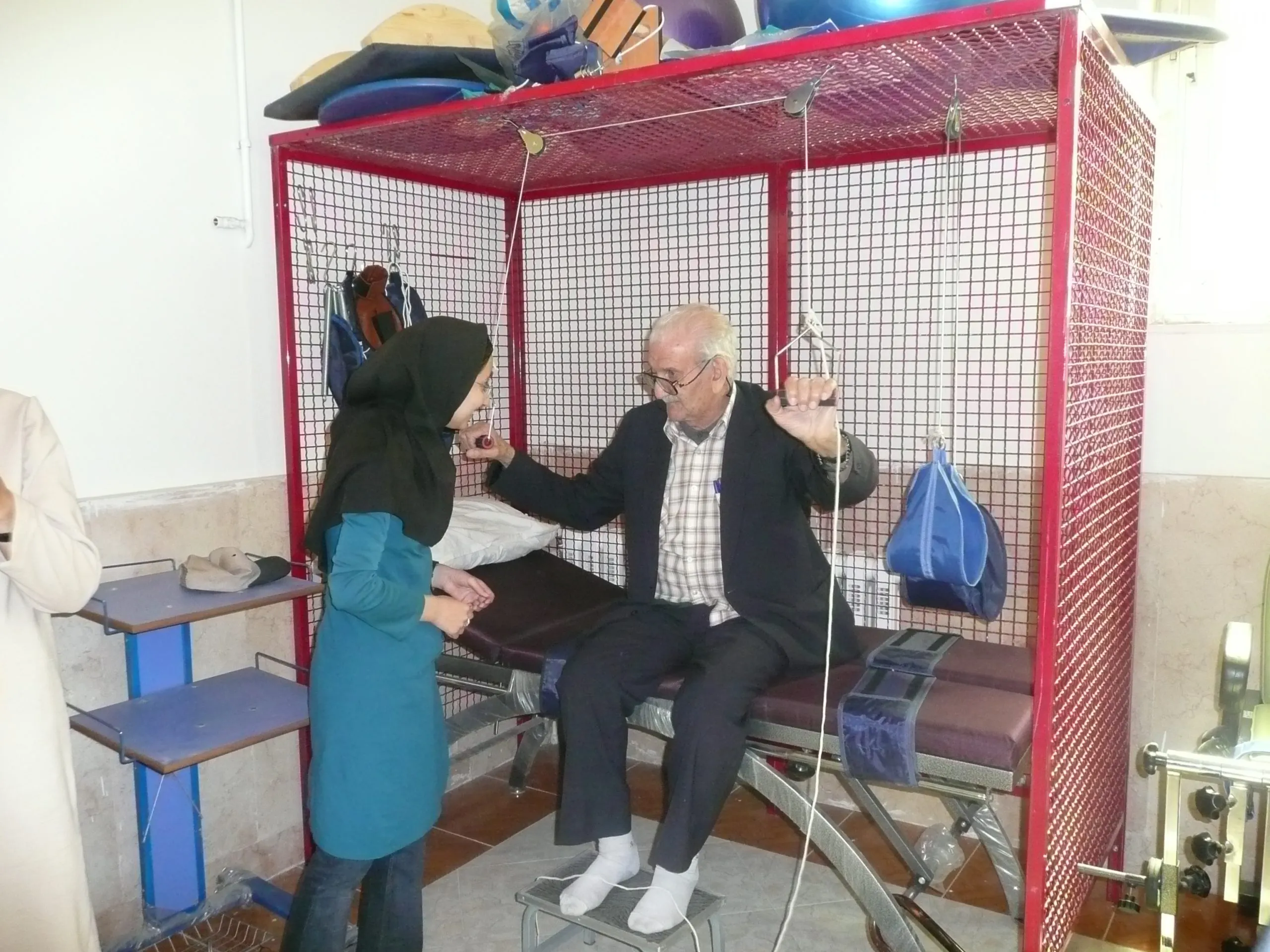 A physiotherapist guides an elderly man through pulley exercises in the day centre's therapy frame