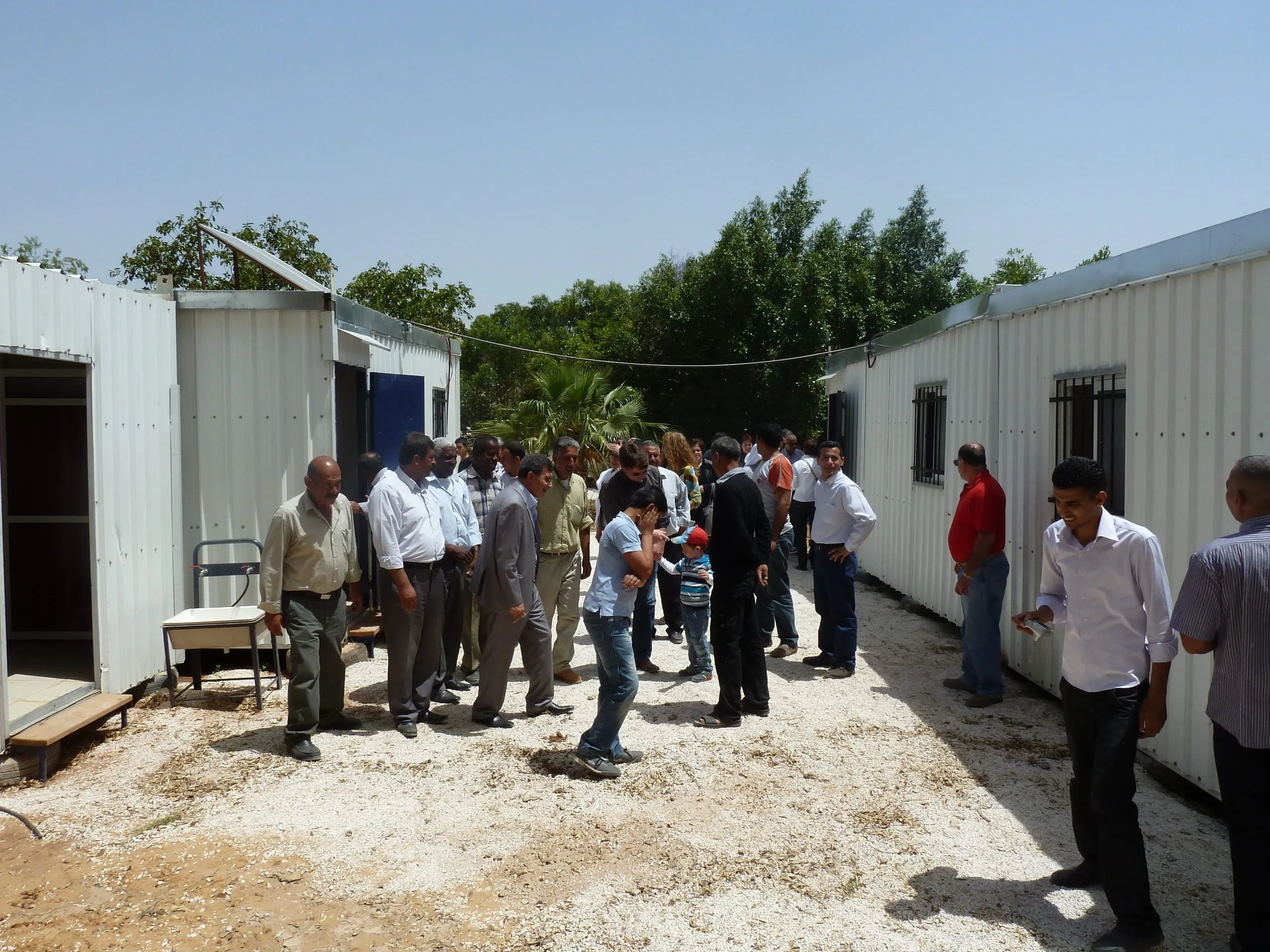 Visitors and villagers walking between the white prefabricated kindergarten units