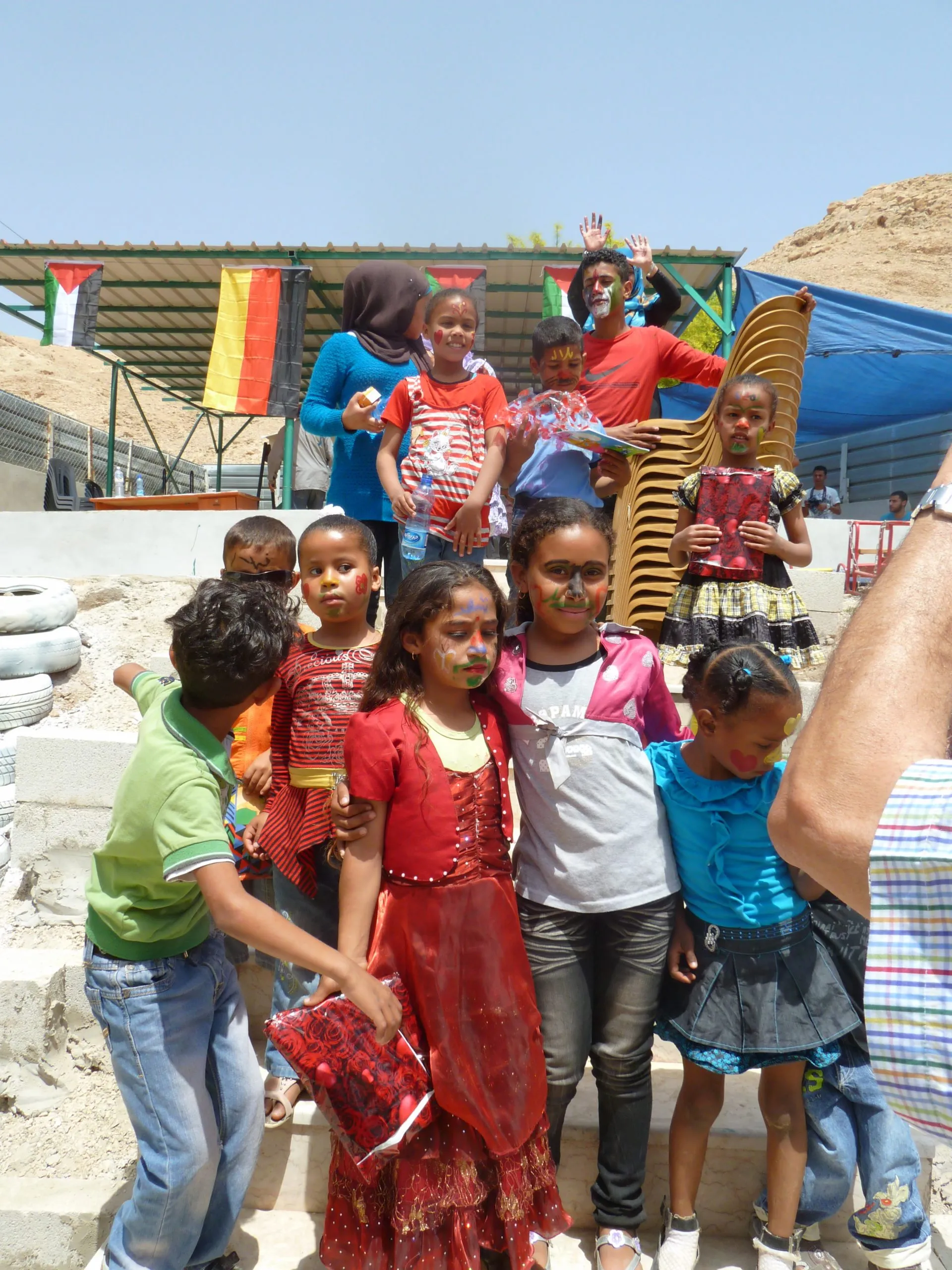 Children with painted faces on the steps at the opening celebration, Palestinian and German flags strung above