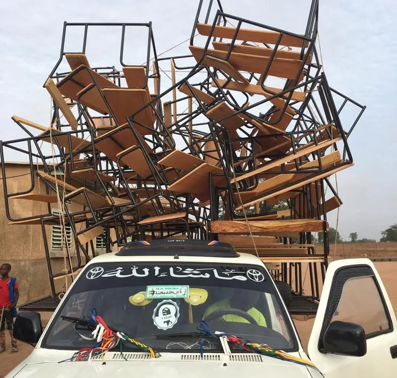 A pickup truck loaded high with school desks and benches for delivery