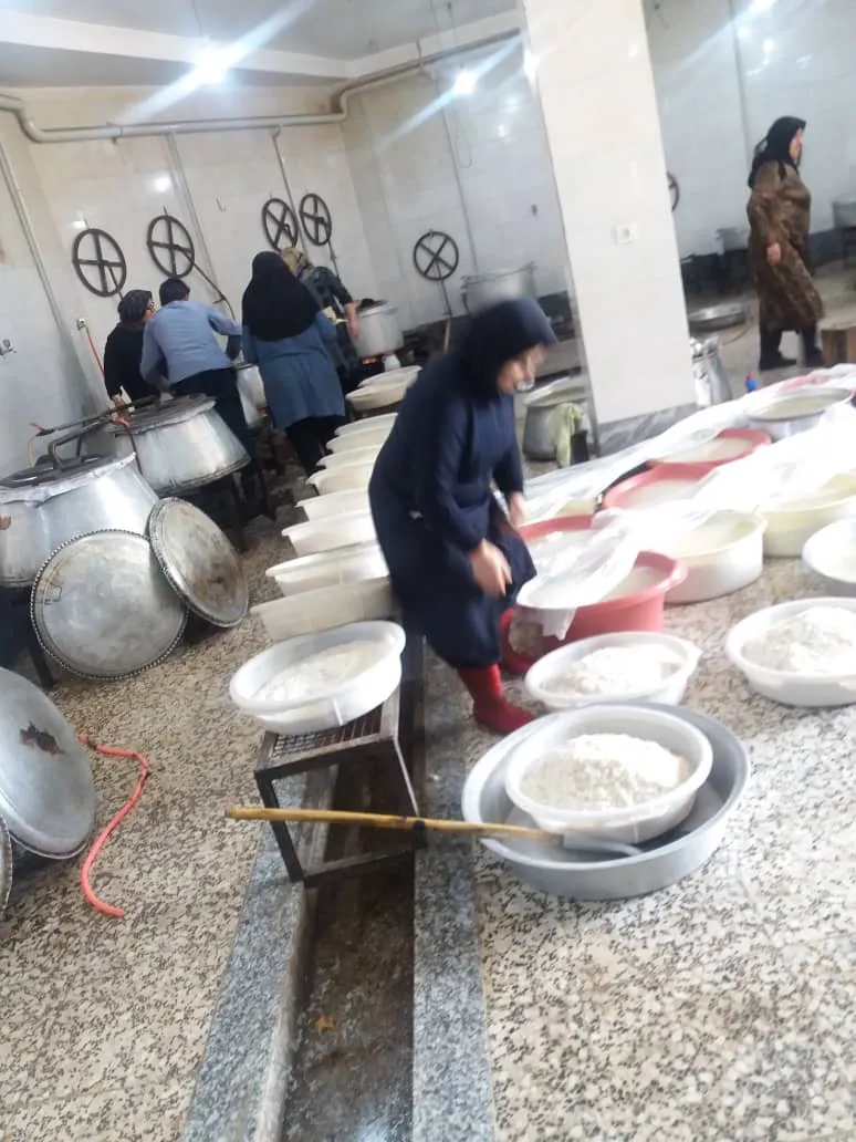 Women at work in the large kitchen among cooking pots and bowls of rice