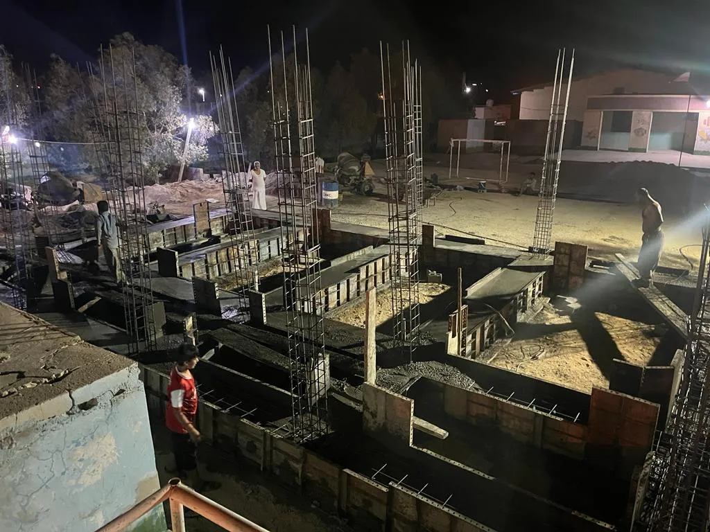 Night-time construction work on the new building: reinforcement cages and formwork under floodlights