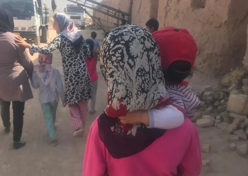 A child carried on a girl's back as the group walks through the brickworks, lorries behind them