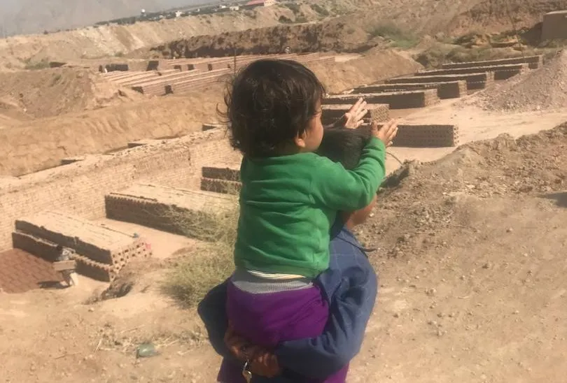 A small child held up to look out over the brick kiln yard and its rows of drying bricks