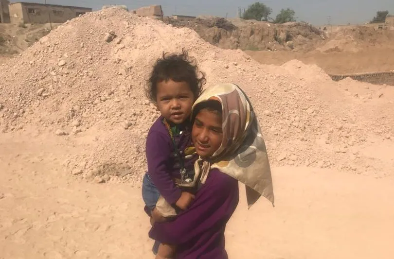 A girl carrying a toddler in front of the sand heaps at the brickworks