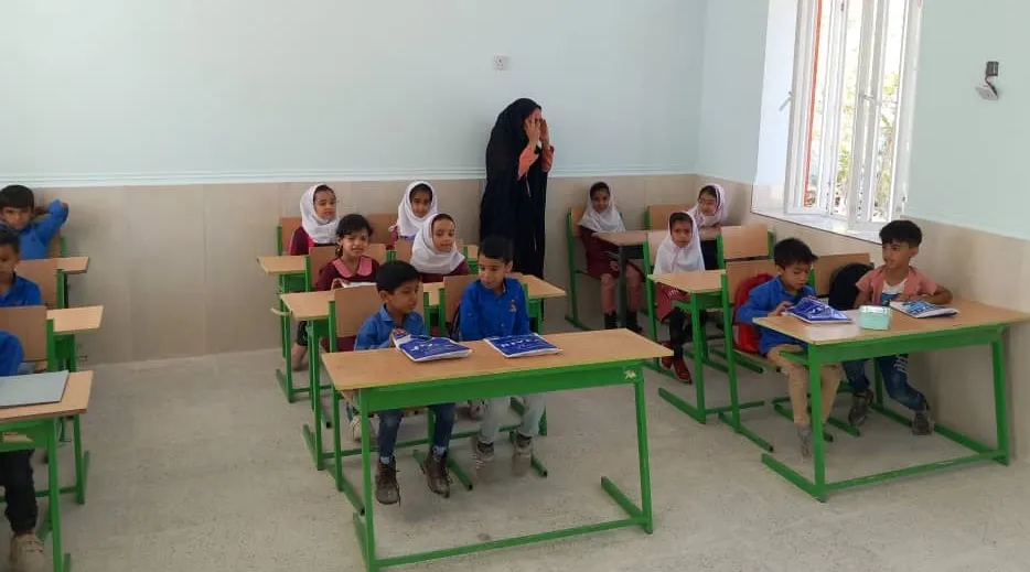 Pupils at new green desks in a bright classroom, a teacher standing at the back