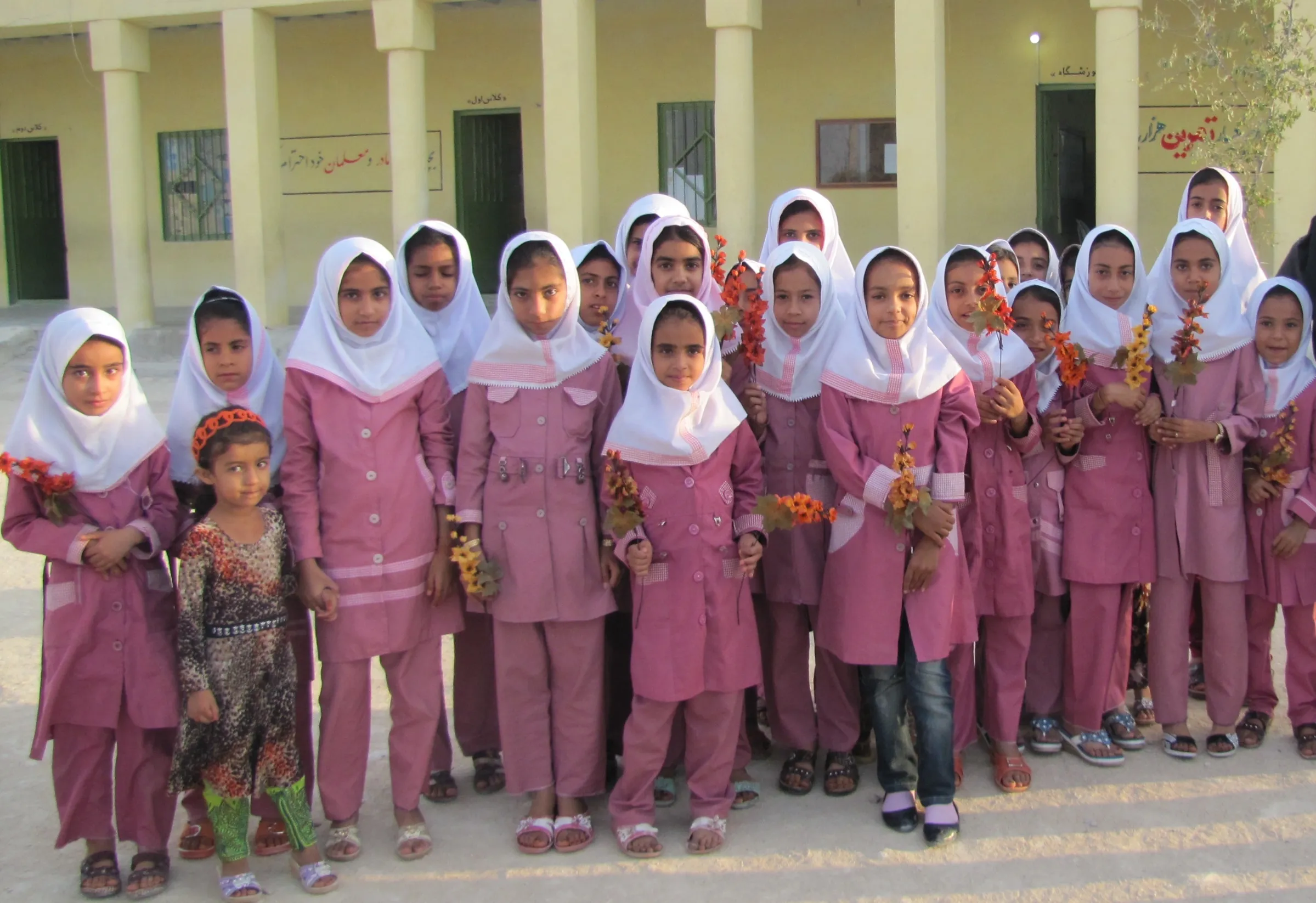 Schoolgirls in pink uniforms and white headscarves standing outside the school holding flowers